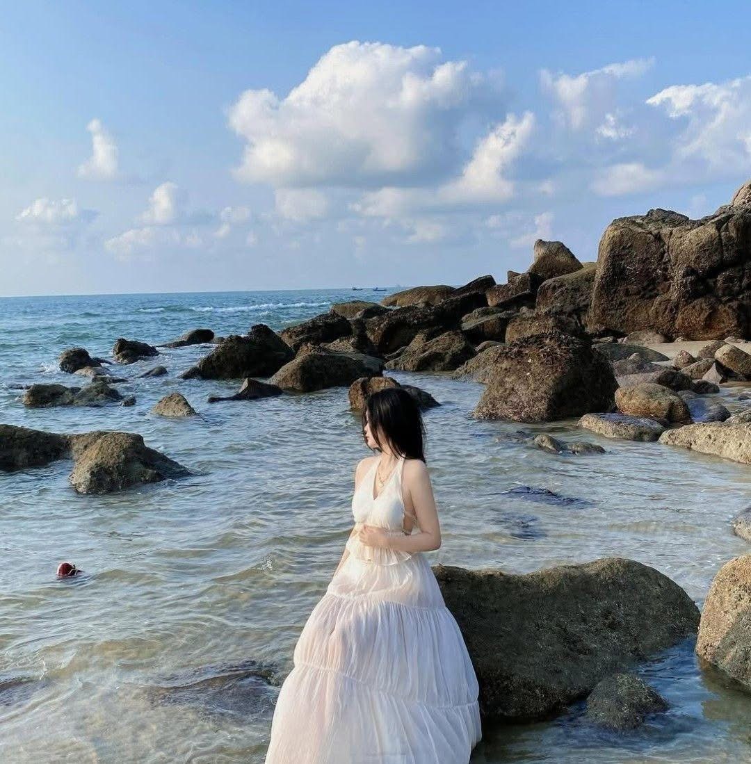 The girl wearing a white dress is sitting on a coastal rock